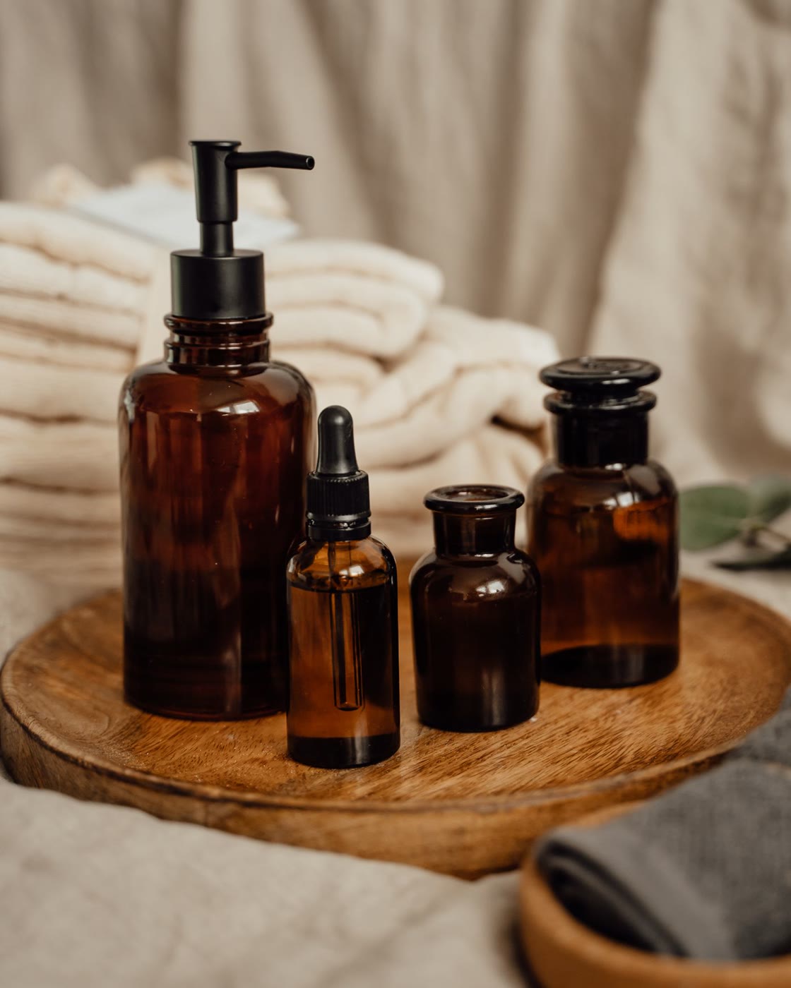A skincare line: pump bottle, serum dropper and two jars on a wooden tray